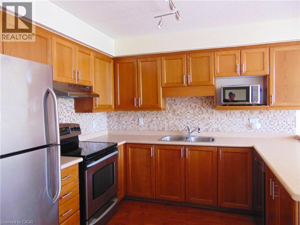 Kitchen featuring wood-finish cabinetry, neutral countertops, and a tiled backsplash - 214 Snowdrop Crescent, Kitchener, ON - Indoor Photo Showing Kitchen With Double Sink
