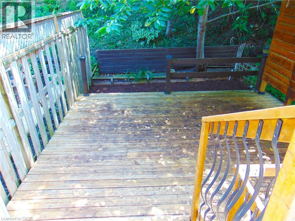 Wood deck featuring a light-toned wooden fence, integrated balusters, a wooden handrail with wrought iron accents, and bordering landscaping with mature trees - 214 Snowdrop Crescent, Kitchener, ON