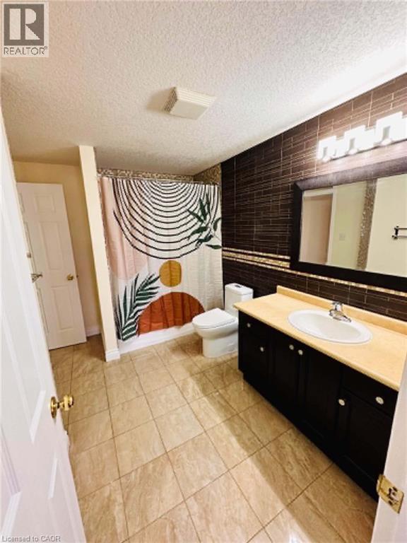 Bathroom featuring tiled flooring, a dark wood-finish vanity with an integrated sink, a full wall mirror, and a tiled shower surround - 214 Snowdrop Crescent, Kitchener, ON