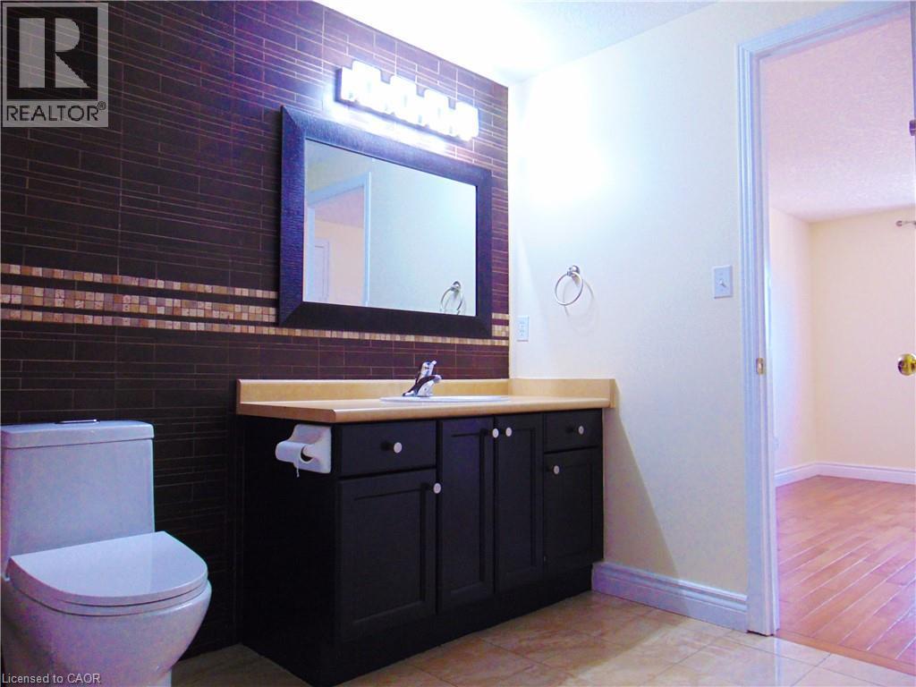 Bathroom featuring a dark subway tile accent wall with a decorative mosaic band, a black vanity with a light-colored countertop, and a rectangular framed mirror with vanity lighting - 214 Snowdrop Crescent, Kitchener, ON