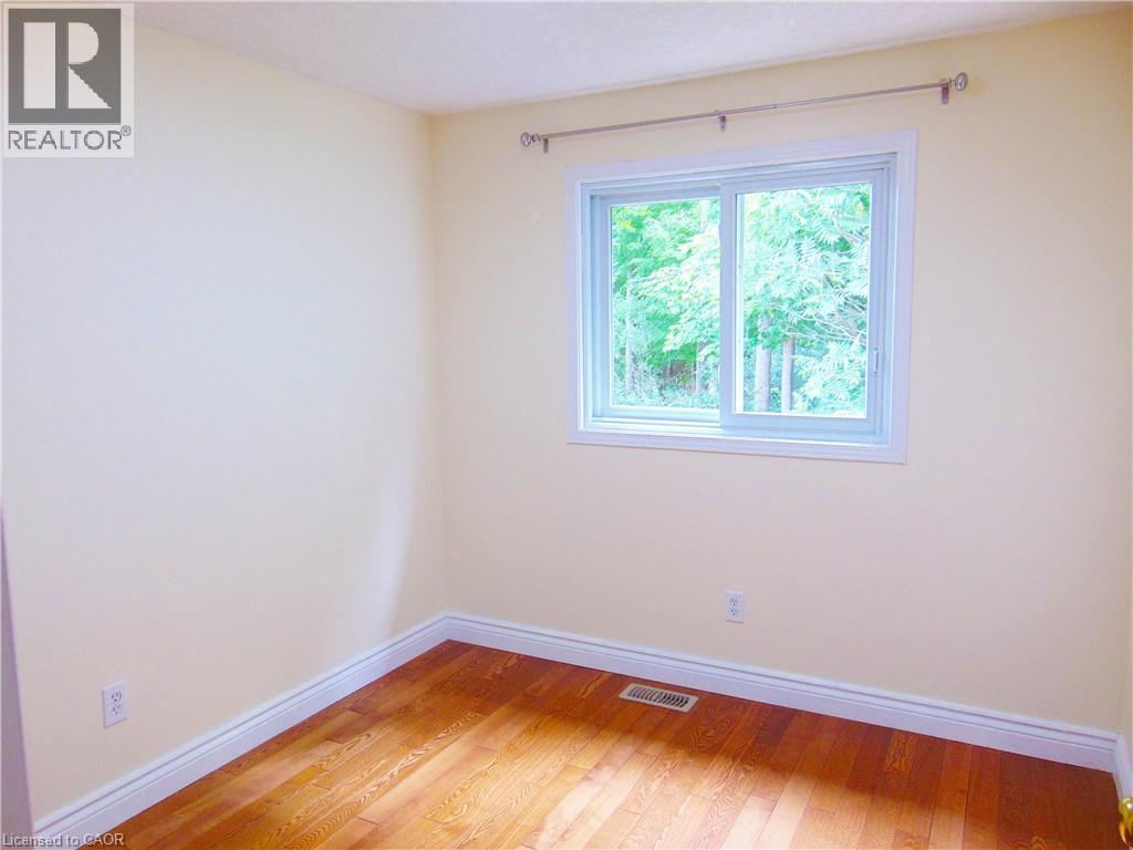 Bedroom featuring wood-finish flooring, white baseboards, and a bright window with a white frame - 214 Snowdrop Crescent, Kitchener, ON