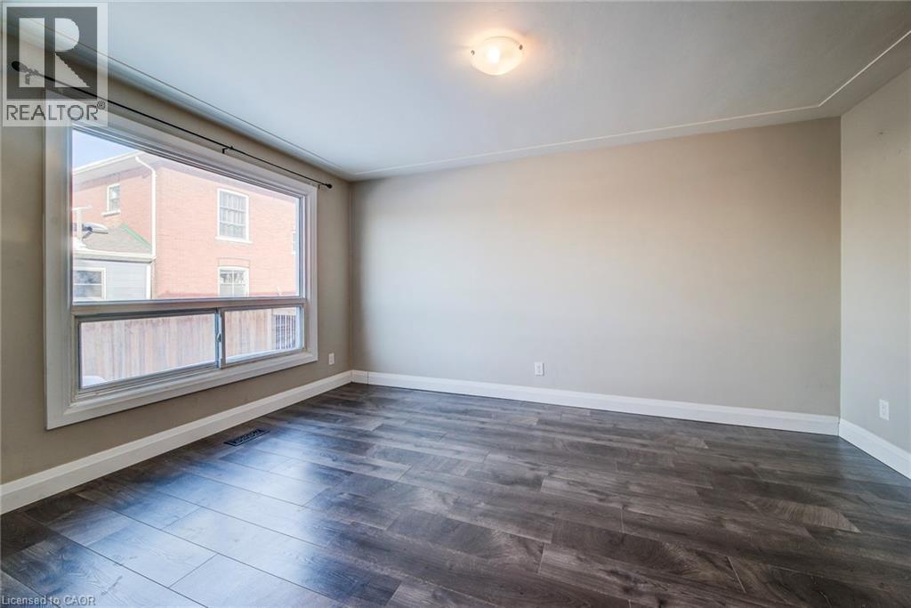 Spacious room featuring wood-finish flooring, a large multi-pane window, neutral wall paint, white trim, and a ceiling-mounted light fixture - 415-435 Garden Street Unit# 421, Cambridge, ON