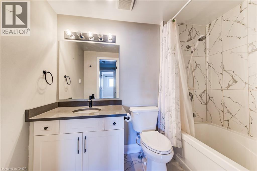 Bathroom featuring a single white vanity with a dark countertop, an integrated sink with a matte black faucet, and a large wall mirror with overhead lighting - 415-435 Garden Street Unit# 421, Cambridge, ON