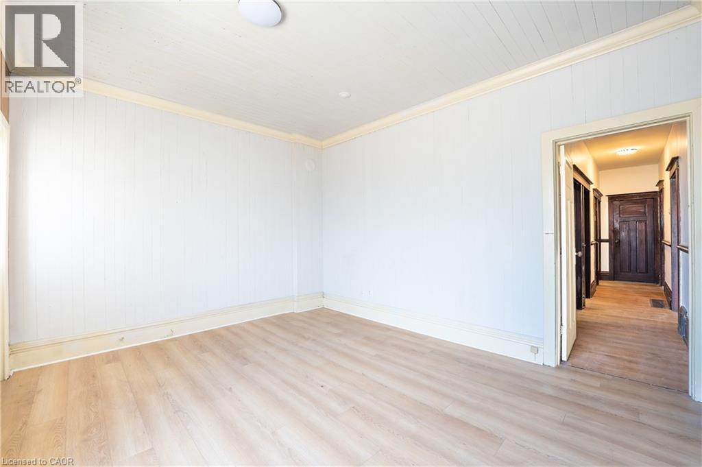Room featuring vertical paneling walls, wood-finish flooring, white baseboards, and crown molding - 1274 Barton Street E, Hamilton, ON