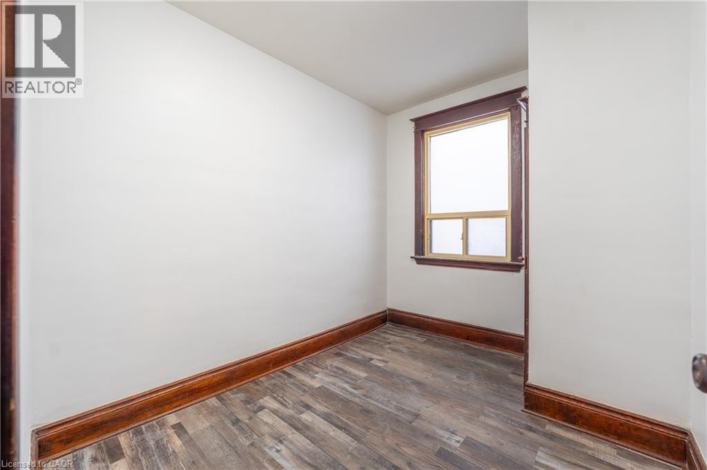 Dedicated room featuring wood-finish flooring, a window with wood trim, white walls, and dark wood baseboards - 1274 Barton Street E, Hamilton, ON