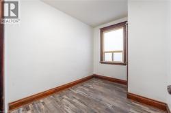 Dedicated room featuring wood-finish flooring, a window with wood trim, white walls, and dark wood baseboards -