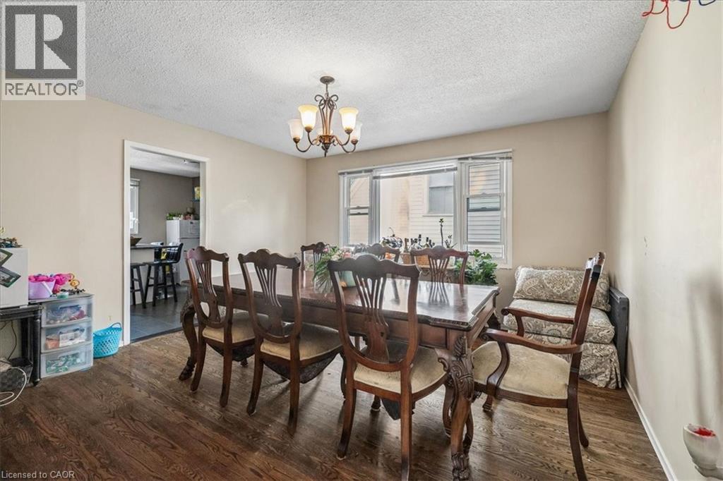 Dining area featuring wood-finish flooring, a multi-bulb chandelier, and a large window with horizontal blinds - 80 Maclennan Avenue, Hamilton, ON