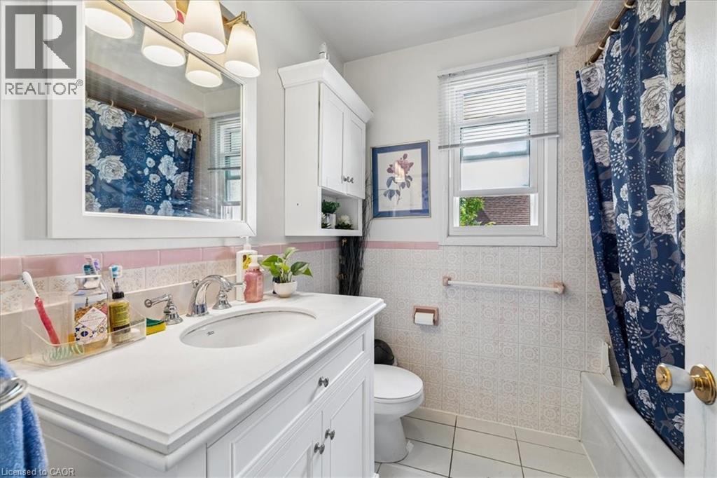 Bathroom featuring a white vanity with an integrated sink, built-in medicine cabinet, tiled walls with a pink accent stripe, and a window providing natural light - 80 Maclennan Avenue, Hamilton, ON