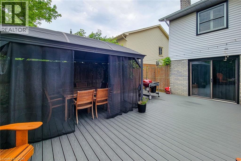 Spacious outdoor deck featuring gray composite decking, a screened gazebo with a dining set, and a sliding glass door entry to the interior - 29 Woodside Square, Fonthill, ON - Outdoor With Deck Patio Veranda With Exterior