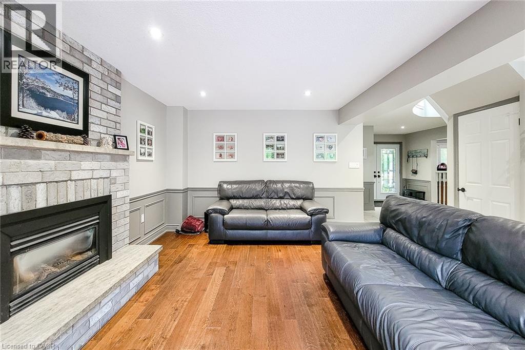 Living area featuring a light-colored brick fireplace with hearth, recessed lighting, wood-finish flooring, and wainscoting - 29 Woodside Square, Fonthill, ON - Indoor Photo Showing Living Room With Fireplace