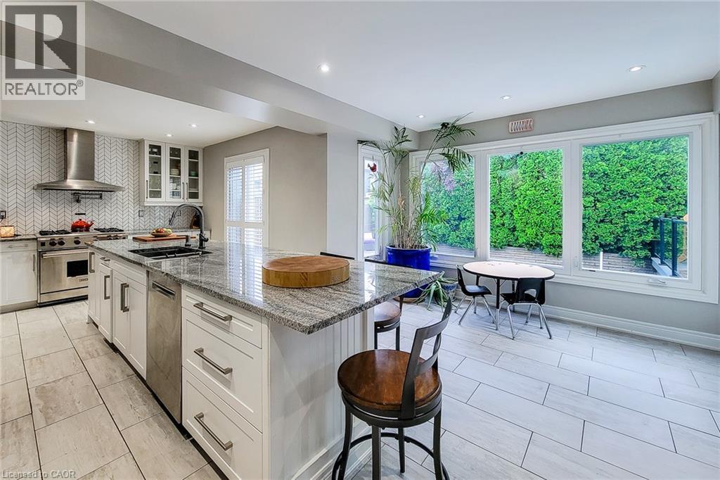 Kitchen featuring a large island with a stone countertop, white shaker cabinetry, stainless steel appliances, and a herringbone-patterned tile backsplash - 29 Woodside Square, Fonthill, ON - Indoor Photo Showing Kitchen With Upgraded Kitchen
