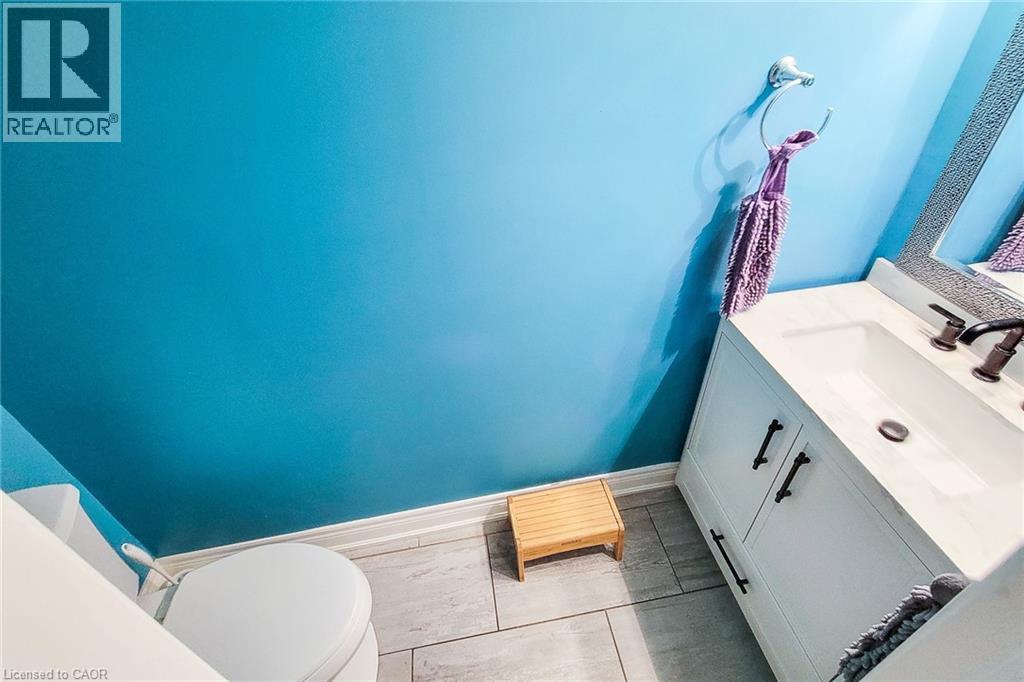 Modern bathroom featuring a white vanity with two cabinet doors and a single drawer, a white integrated sink with a dark bronze faucet, and a decorative framed mirror - 29 Woodside Square, Fonthill, ON - Indoor Photo Showing Bathroom
