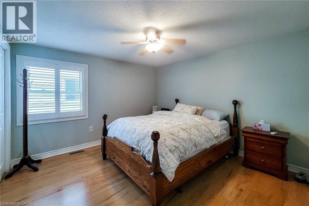 Bedroom featuring wood-finish flooring, a ceiling fan with integrated lighting, and a window with plantation shutters - 29 Woodside Square, Fonthill, ON - Indoor Photo Showing Bedroom