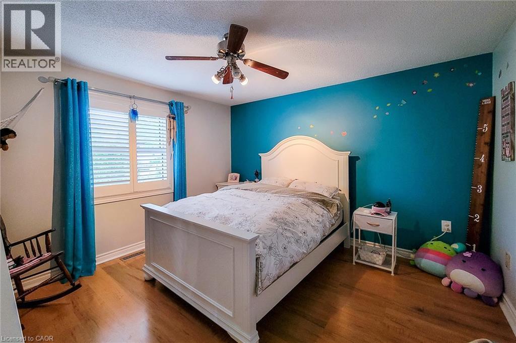 Bedroom featuring wood-finish flooring, a ceiling fan with integrated lighting, and a window fitted with white plantation shutters - 29 Woodside Square, Fonthill, ON - Indoor Photo Showing Bedroom