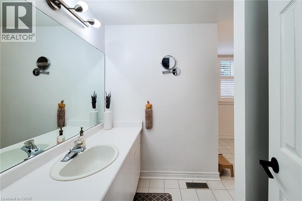 Bathroom vanity featuring an integrated sink, expansive wall mirror, contemporary light fixture, and ceramic tile flooring - 29 Woodside Square, Fonthill, ON - Indoor Photo Showing Bathroom