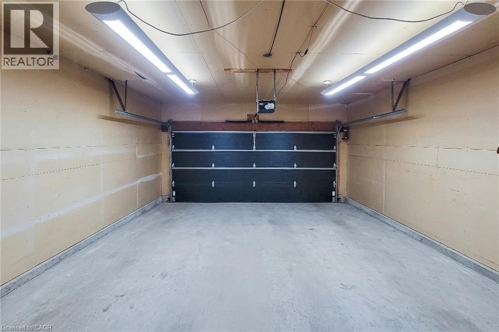 Spacious garage featuring a concrete floor, two overhead linear light fixtures, a black sectional garage door, and an overhead garage door opener - 29 Woodside Square, Fonthill, ON - Indoor Photo Showing Garage