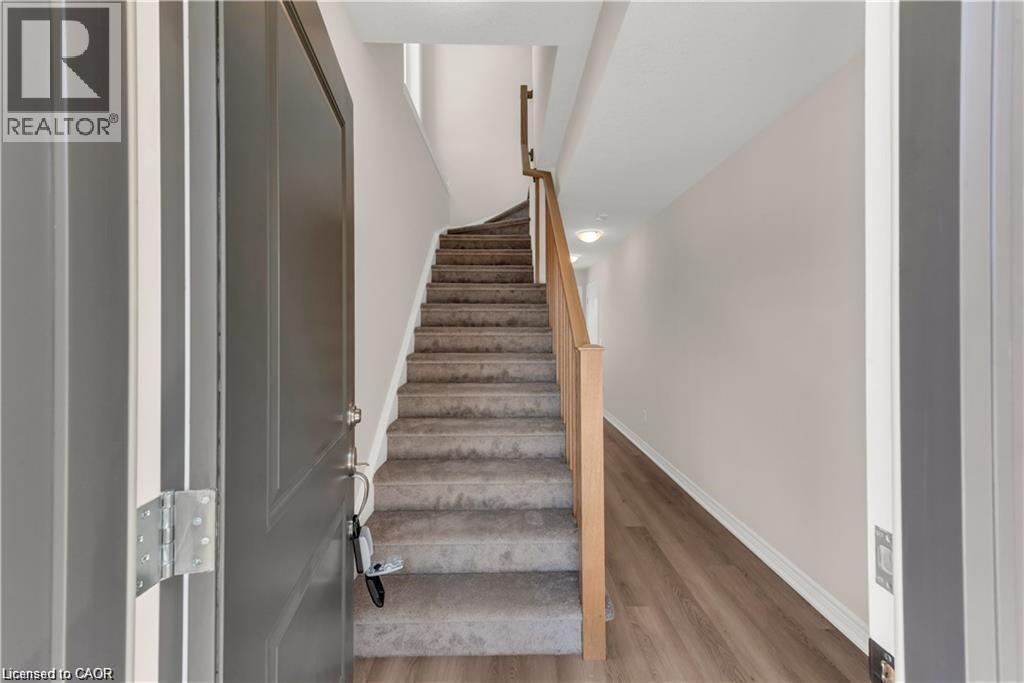 Entryway featuring a contemporary gray front door, light wood-finish flooring, and a carpeted staircase with a natural wood railing - 19 Picardy Drive Unit# 9, Hamilton, ON