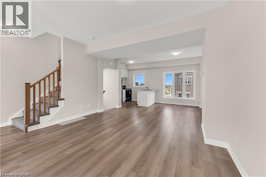 Spacious open-concept living area featuring wood-finish flooring throughout, a carpeted staircase with wood handrails, and ample natural light from multiple windows - 19 Picardy Drive Unit# 9, Hamilton, ON
