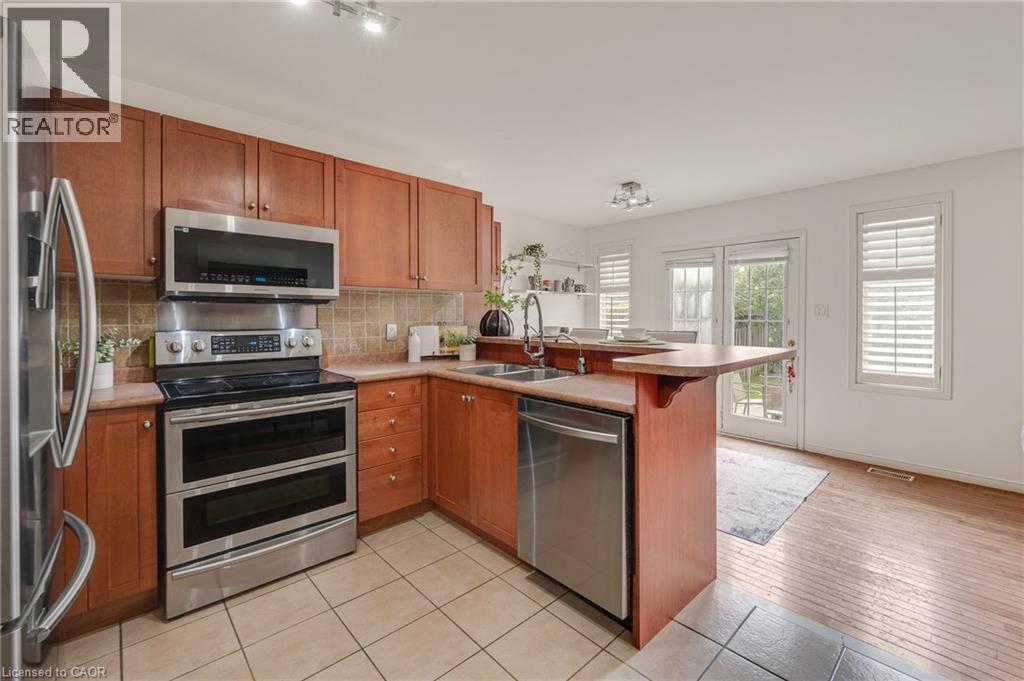 Kitchen featuring stainless steel appliances, wood cabinetry, a tile backsplash, and a breakfast bar - 409 Jacqueline Boulevard, Hamilton, ON