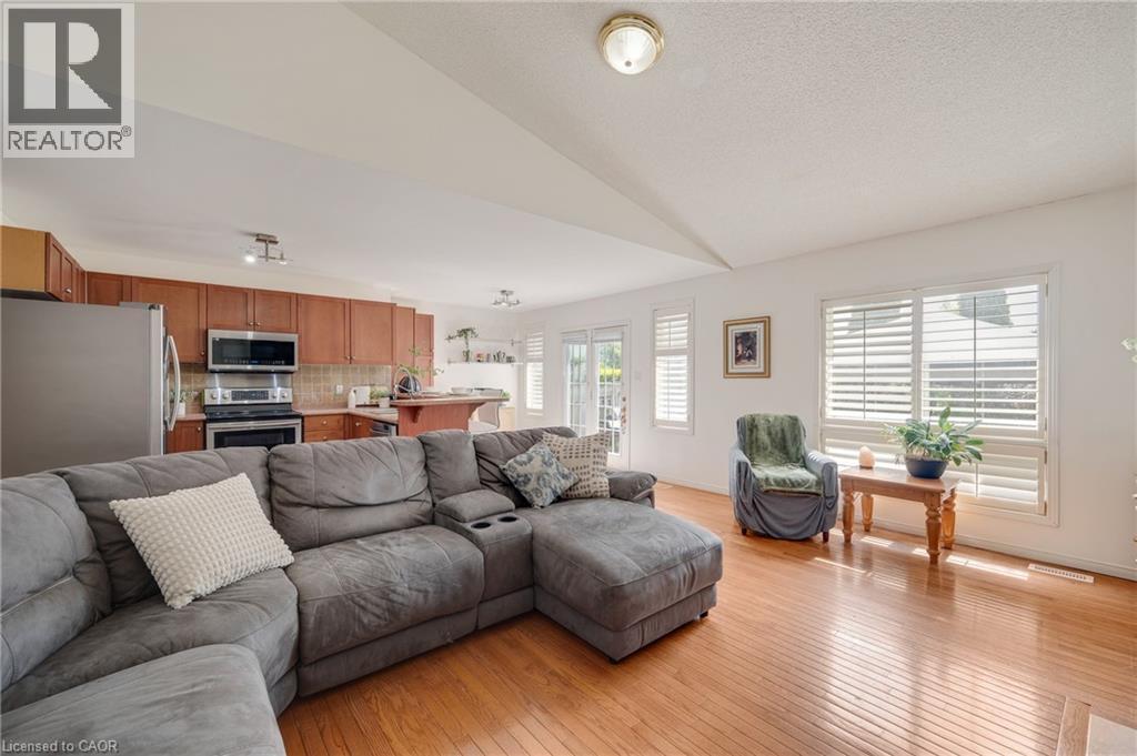 Open-concept living space featuring wood-finish flooring, white walls, and a kitchen with warm wood cabinetry and stainless steel appliances - 409 Jacqueline Boulevard, Hamilton, ON