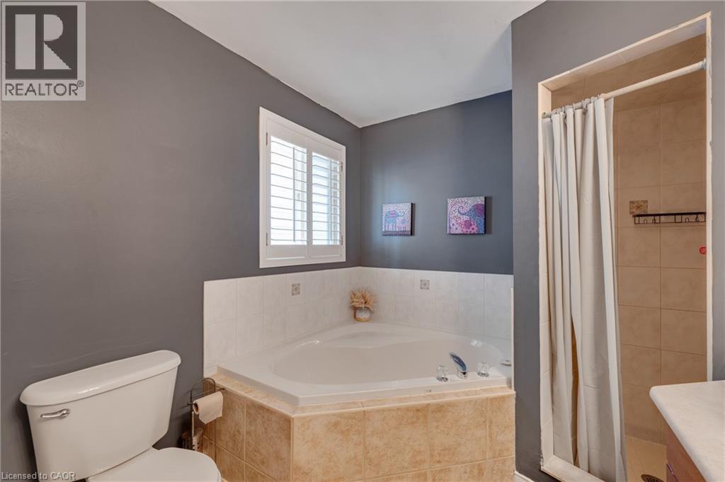 Corner soaking tub with a tiled surround, plantation-shutter window, and a separate shower enclosure with full tile walls - 409 Jacqueline Boulevard, Hamilton, ON