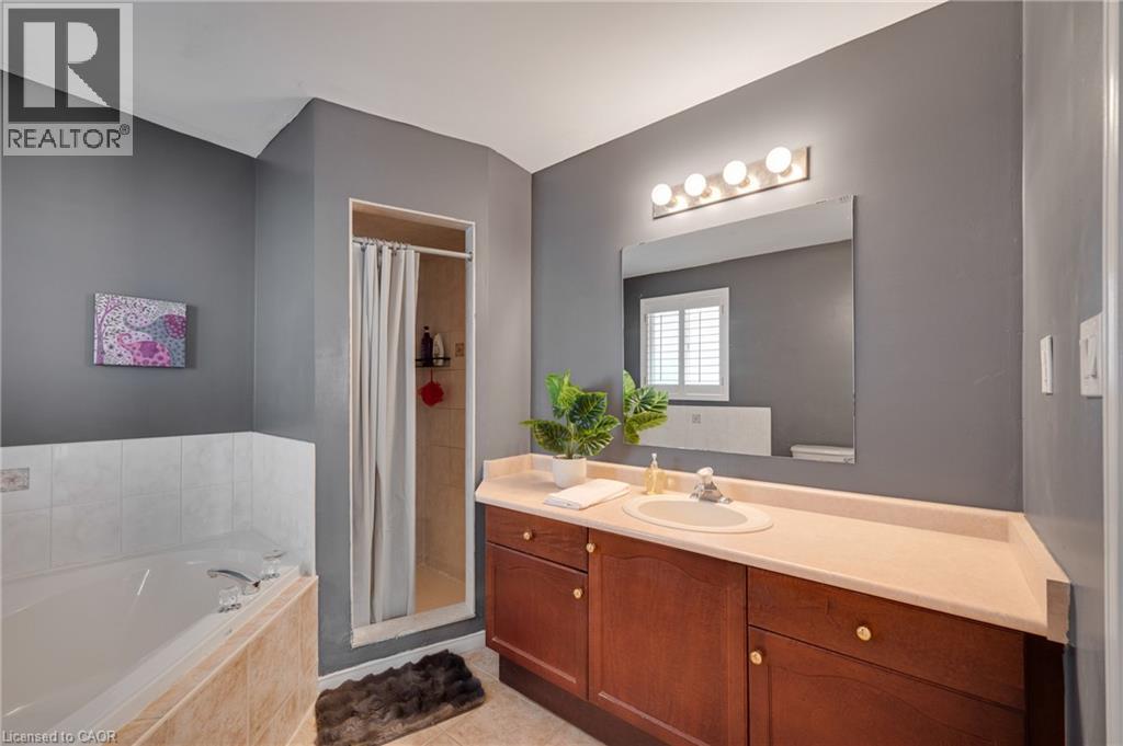 Bathroom featuring a built-in tub with tiled surround, a separate shower stall with tiled walls, a wood-finish vanity with an integrated sink, a light-toned countertop, and a large wall-mounted mirror - 409 Jacqueline Boulevard, Hamilton, ON