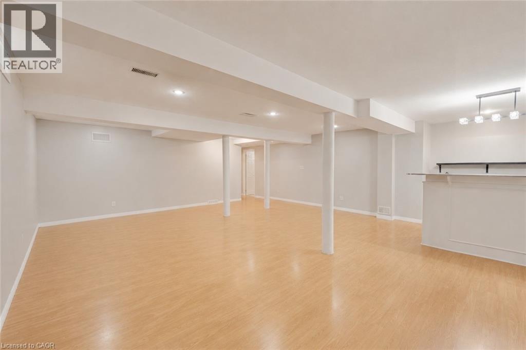 Expansive finished lower level featuring light wood-finish flooring, recessed lighting, and a built-in wet bar with white cabinetry and a light-toned countertop. Furniture has been removed. - 409 Jacqueline Boulevard, Hamilton, ON