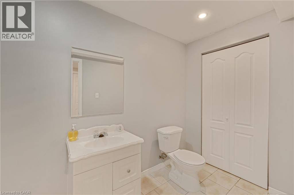 Brightly painted interior featuring a white vanity with integrated sink, rectangular mirror, and a modern toilet - 409 Jacqueline Boulevard, Hamilton, ON