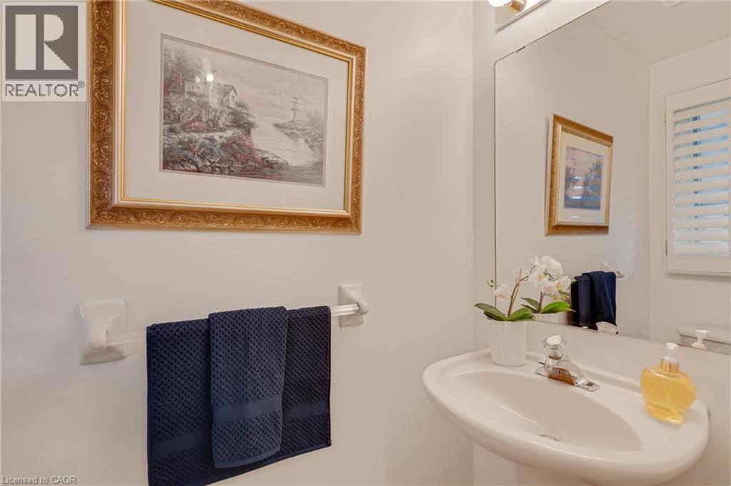Pedestal sink with chrome faucet, large vanity mirror, and wall-mounted light fixture - 409 Jacqueline Boulevard, Hamilton, ON