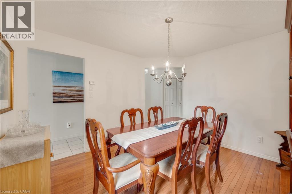 Bright dining area featuring wood-finish flooring, a contemporary chandelier, and direct access to another room with tiled flooring - 409 Jacqueline Boulevard, Hamilton, ON