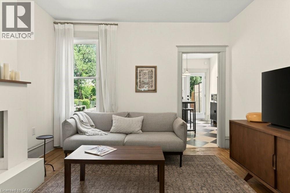 Bright living space featuring a window with exterior green foliage, light-toned walls, and wood-finish flooring - 148 Dundurn Street N, Hamilton, ON