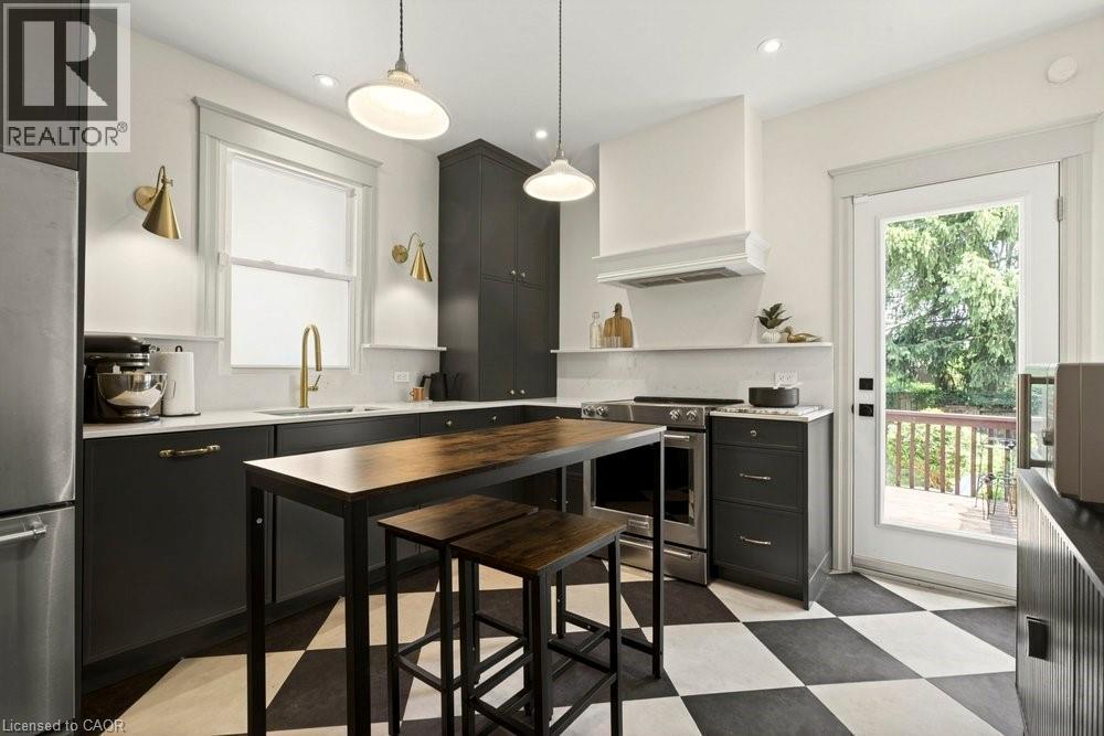 Modern kitchen featuring a checkered floor, dark cabinetry, white countertops, and stainless steel appliances - 148 Dundurn Street N, Hamilton, ON