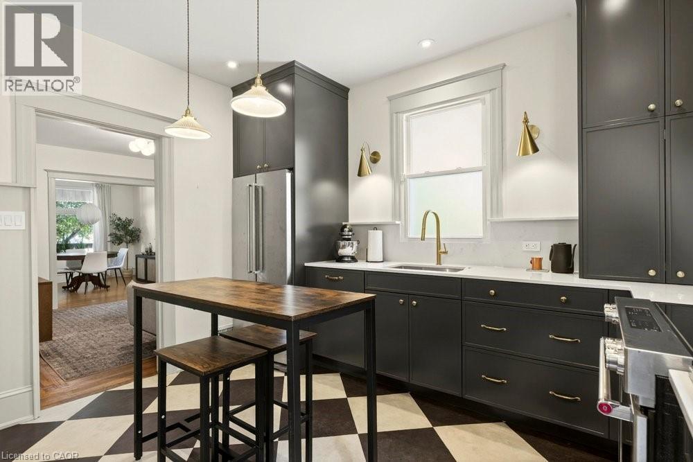 Kitchen featuring dark cabinetry with gold-toned hardware, stainless steel refrigerator, white countertops, and checkerboard flooring - 148 Dundurn Street N, Hamilton, ON