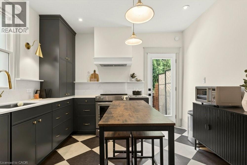 Kitchen featuring black and white checkerboard flooring, dark cabinetry with brass hardware, stainless steel appliances, and a wood-finish island - 148 Dundurn Street N, Hamilton, ON