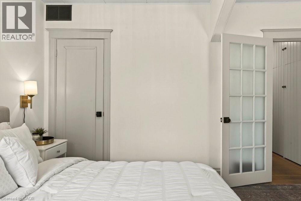 Interior room featuring a paneled door with dark hardware, a white multi-pane door with frosted glass, and a wall-mounted sconce with a gold-tone finish - 148 Dundurn Street N, Hamilton, ON