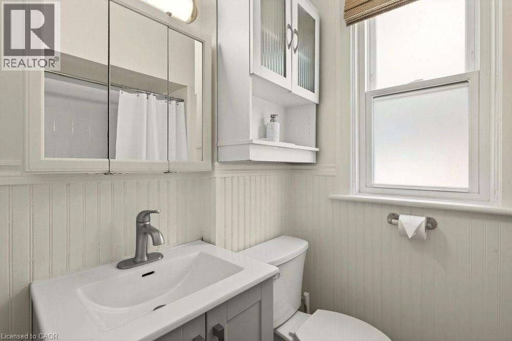 Bathroom featuring a single-sink vanity with a chrome faucet, beadboard wainscoting, an overhead mirrored medicine cabinet, and a window with a privacy film - 148 Dundurn Street N, Hamilton, ON