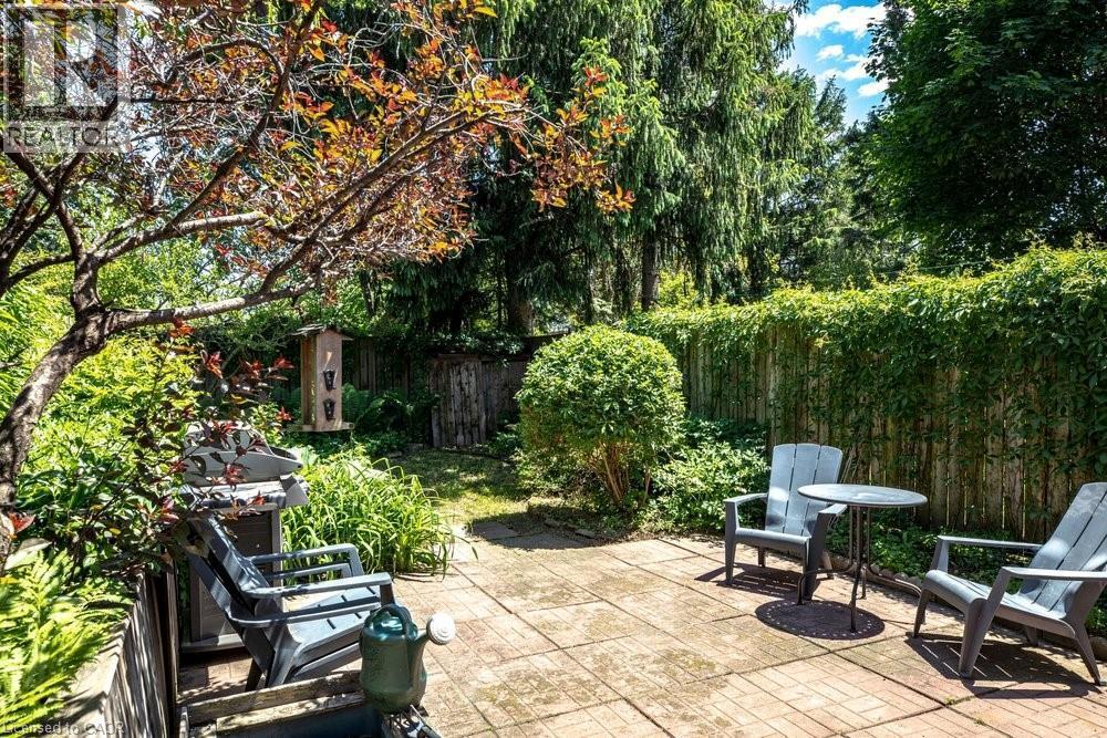 Expansive backyard with a paver patio area, mature trees, lush greenery, and a wood privacy fence - 148 Dundurn Street N, Hamilton, ON