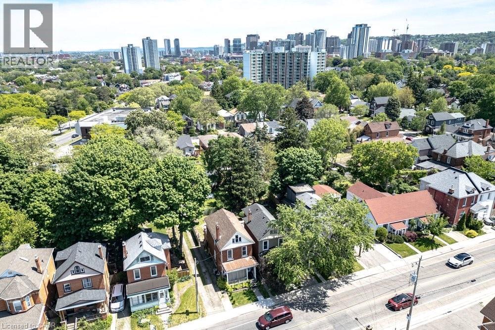Aerial view of a residential street with detached homes featuring various architectural styles, mature trees, and a distant cityscape - 148 Dundurn Street N, Hamilton, ON
