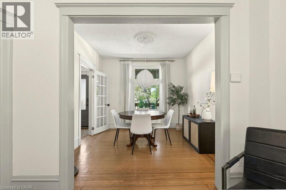 Bright room featuring wood-finish flooring with inlay, white walls, and a window with white curtains - 148 Dundurn Street N, Hamilton, ON