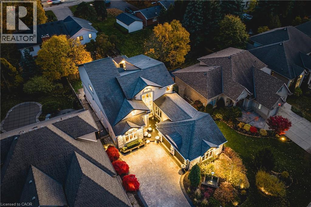 Expansive property featuring a multi-gabled roofline, stone facade accents, a paved driveway, and mature landscaping with accent lighting - 712 Highvalley Road, Ancaster, ON