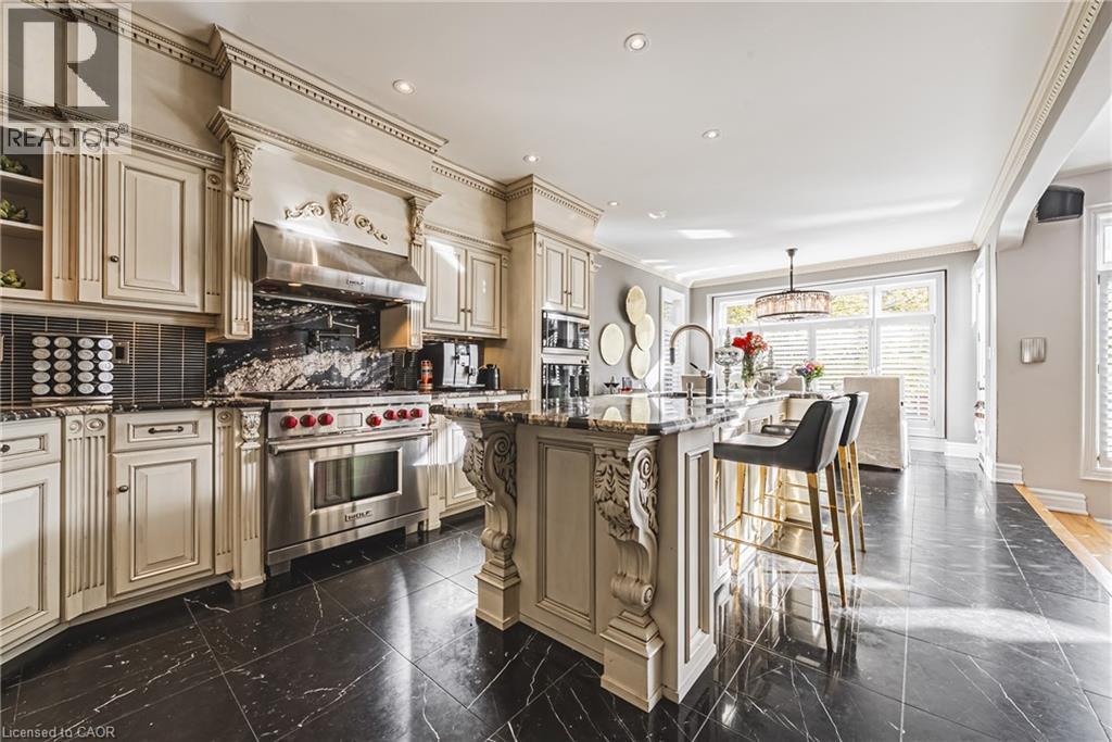 Gourmet kitchen featuring a substantial central island, stainless steel range with matching hood, custom cabinetry, black marble countertops and backsplash, and dark polished tile flooring - 712 Highvalley Road, Ancaster, ON