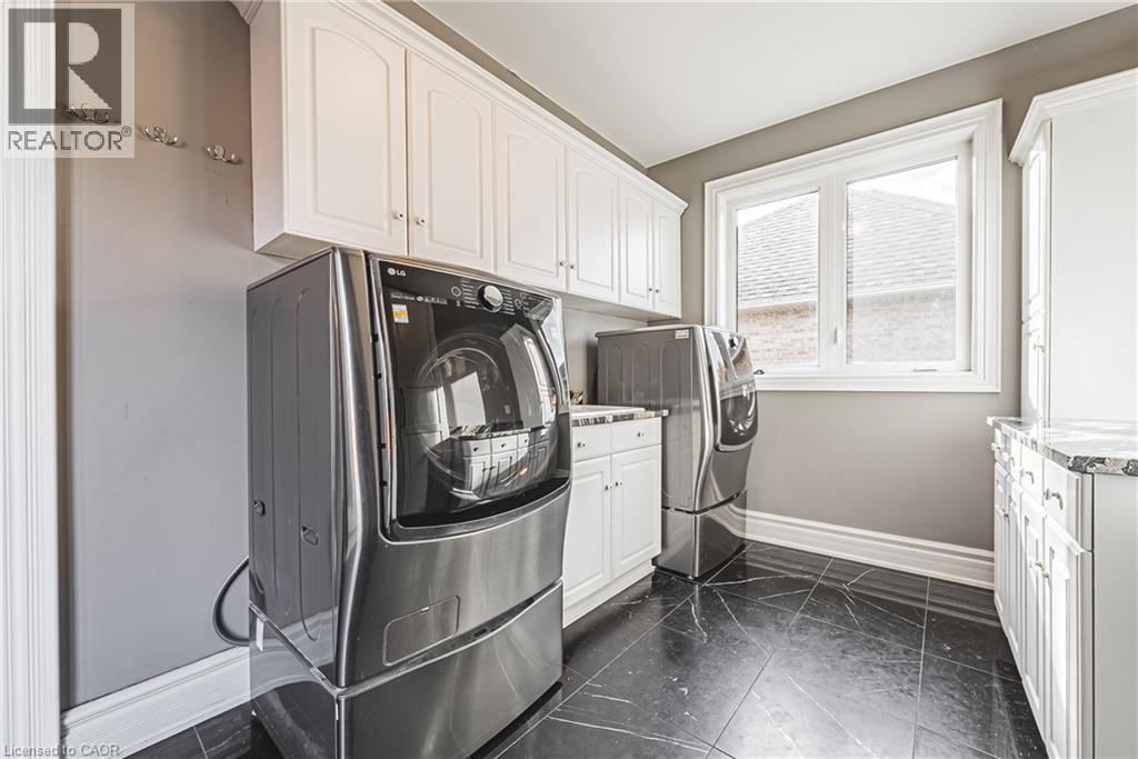 Laundry area featuring white cabinetry, a large window, dark tile flooring, and light gray walls - 712 Highvalley Road, Ancaster, ON