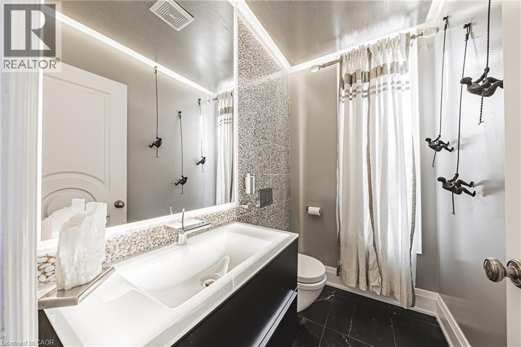 Bathroom featuring a modern vanity with integrated sink, black countertop, and large illuminated mirror - 712 Highvalley Road, Ancaster, ON
