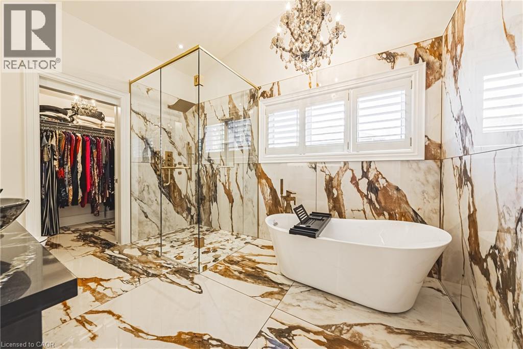 Spacious bathroom featuring large format marble-look tile flooring and walls, a freestanding soaking tub, and a frameless glass shower enclosure with brass-finish hardware - 712 Highvalley Road, Ancaster, ON