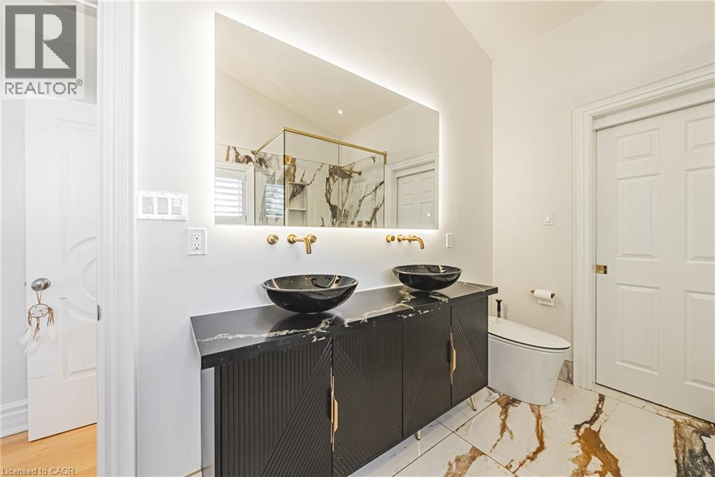 Double vanity featuring vessel sinks, wall-mounted brass fixtures, and a back-lit mirror - 712 Highvalley Road, Ancaster, ON