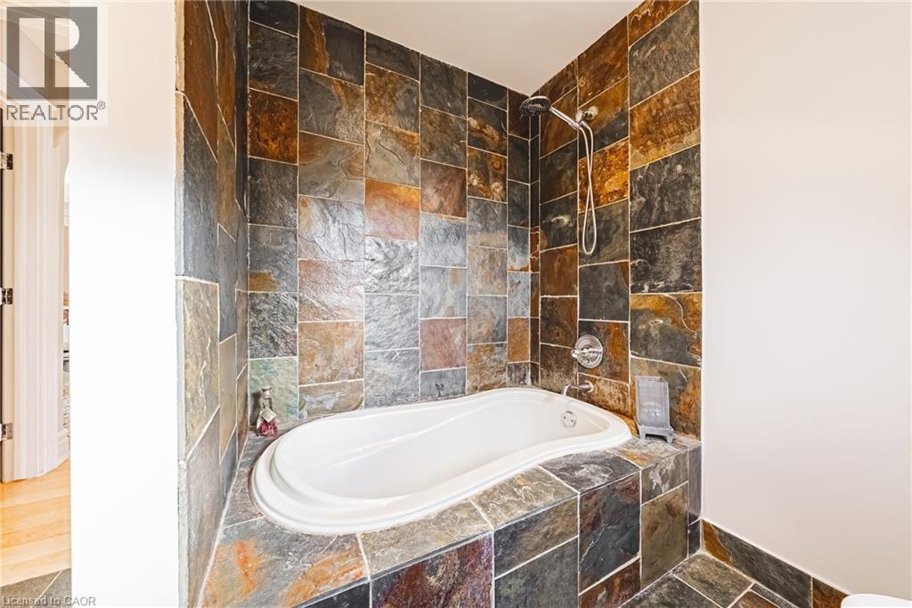 Built-in soaking tub featuring textured tile surround and walls, chrome fixtures, and a handheld showerhead - 712 Highvalley Road, Ancaster, ON