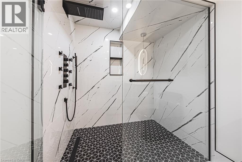 Enclosed shower with full-height glass panels, black geometric floor tiling, and white marble-look wall tiling with dark veining - 712 Highvalley Road, Ancaster, ON