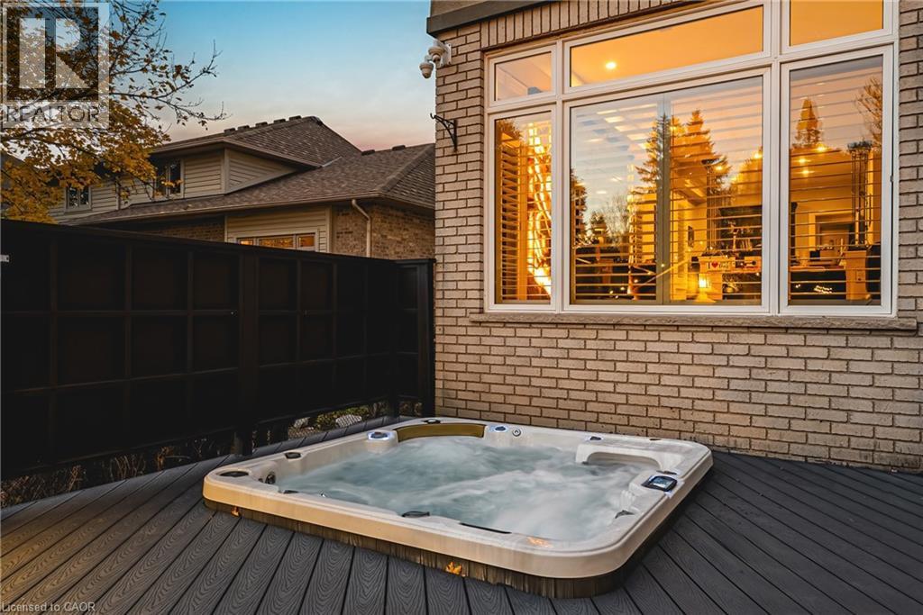 Outdoor hot tub on a composite deck, featuring a brick exterior, large windows with horizontal blinds, and a dark privacy fence - 712 Highvalley Road, Ancaster, ON