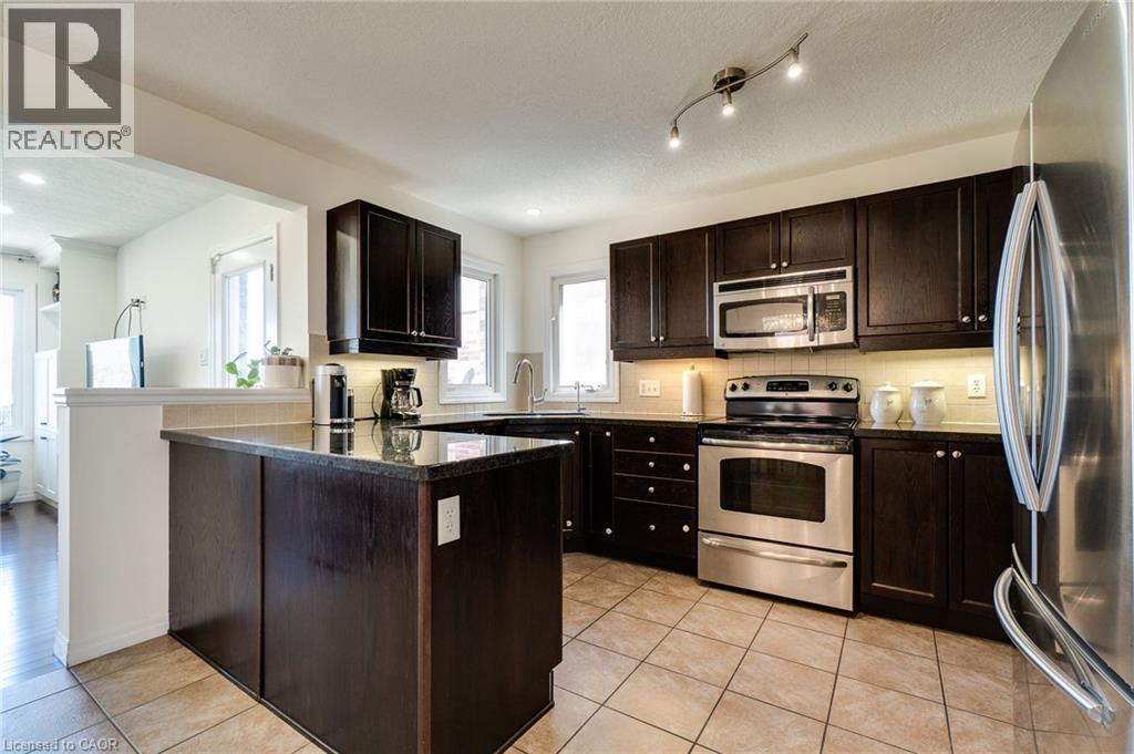 Kitchen featuring dark wood cabinetry, stainless steel appliances, a center island with a dark countertop, and light-toned floor tiles - 928 Dunblane Court, Kitchener, ON