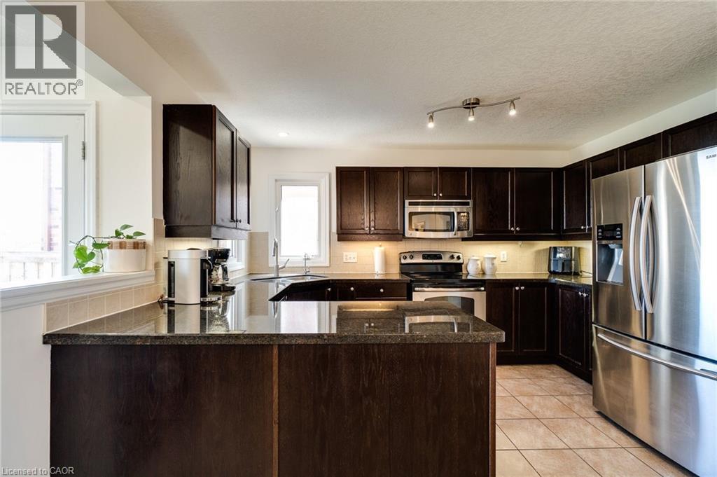 Kitchen featuring dark wood-finish cabinetry, stainless steel appliances, granite-style countertops, and tile flooring - 928 Dunblane Court, Kitchener, ON
